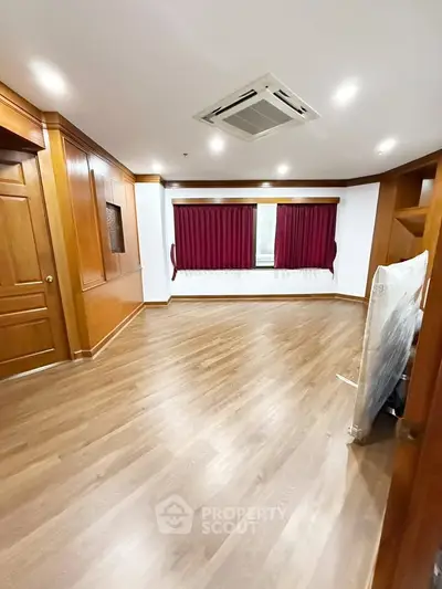 Spacious empty room with wooden flooring and red curtains, ideal for customization.