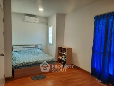 Cozy bedroom with wooden flooring and blue curtains, featuring a bed and storage unit.