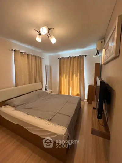 Cozy bedroom with modern lighting and natural light from large windows, featuring a comfortable bed and stylish decor.
