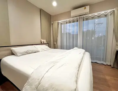 Cozy bedroom with large bed and window view, featuring elegant curtains and modern air conditioning.