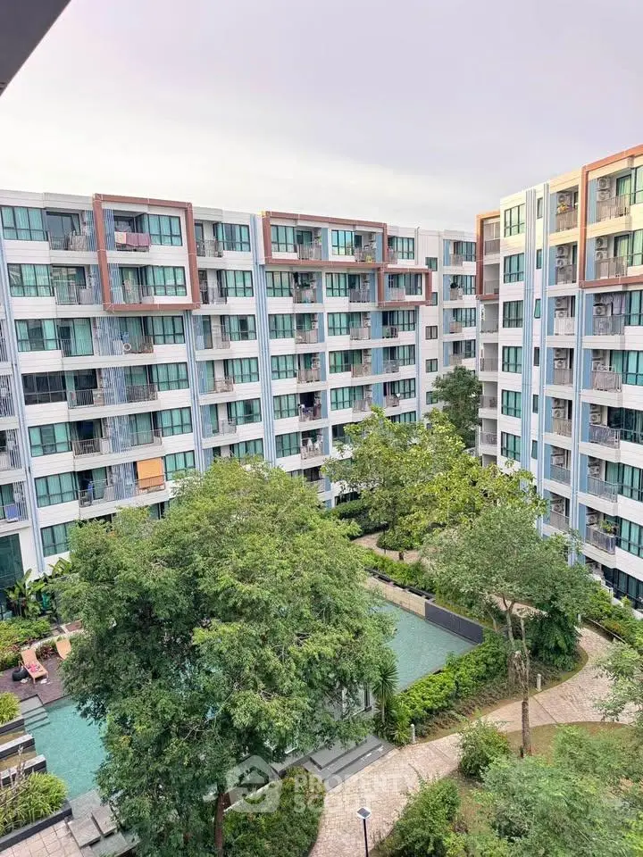 Modern condominium building with lush garden and pool view, offering serene urban living.