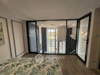 Modern bedroom with large glass doors overlooking a bright living area, featuring stylish decor and natural light.