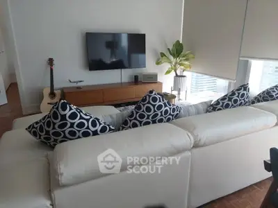 Modern living room with stylish decor, featuring a white sofa, patterned cushions, and a wall-mounted TV.