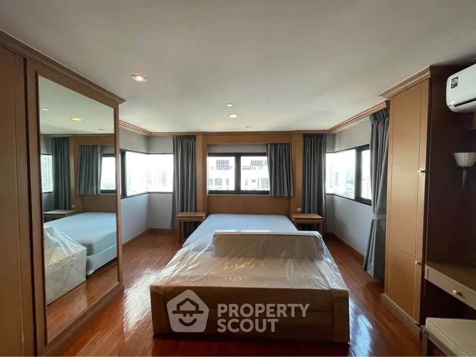 Spacious bedroom with large windows and mirrored wardrobe in modern apartment.