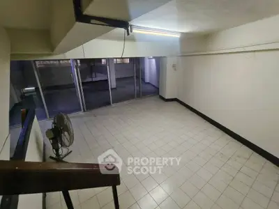 Spacious tiled room with large windows and staircase, ideal for versatile use.