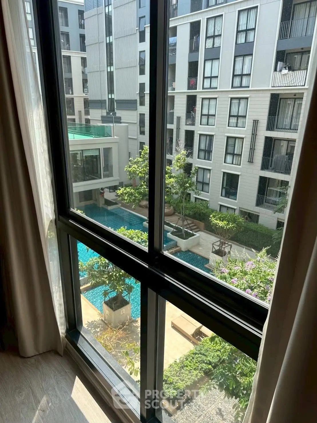 Modern apartment view with pool and garden from window, showcasing urban living elegance.