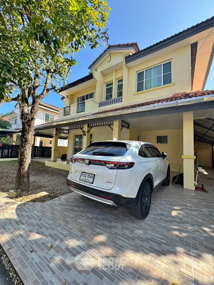 Charming two-story house with carport and lush tree, perfect for family living.