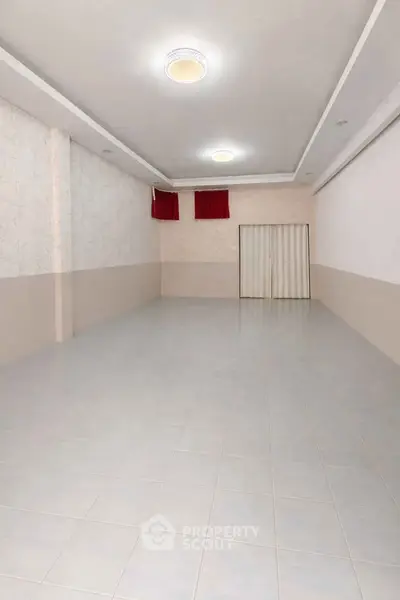 Spacious empty room with tiled flooring and modern lighting, ideal for versatile use.