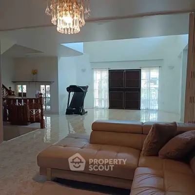 Spacious living room with elegant chandelier and modern treadmill, featuring luxurious leather sofa.