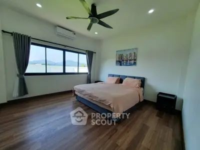 Spacious bedroom with large window and modern decor, featuring a comfortable bed and ceiling fan.