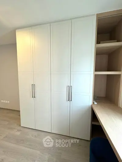Modern bedroom with built-in wardrobe and desk, light wood flooring.