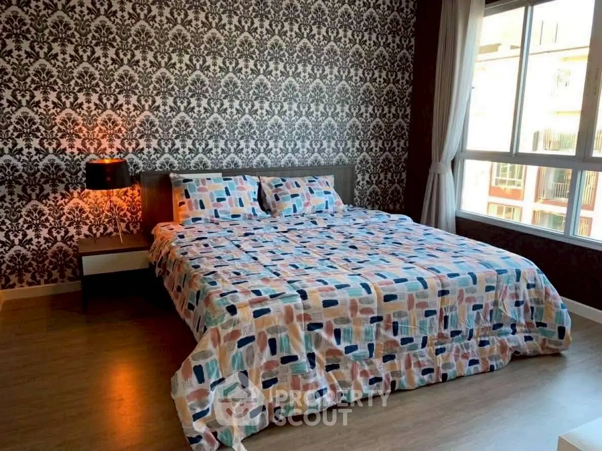 Stylish bedroom with patterned wallpaper and large window for natural light.