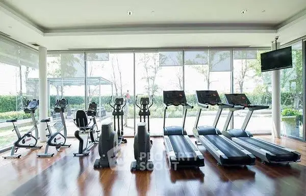 Spacious modern gym with treadmills and exercise bikes, large windows offering garden views.
