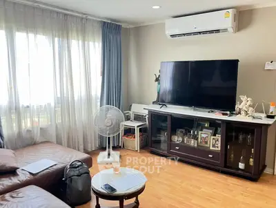 Cozy living room with large TV, air conditioning, and natural light from big windows.