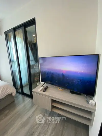 Modern bedroom with sleek TV setup and sliding glass doors leading to a cozy balcony.