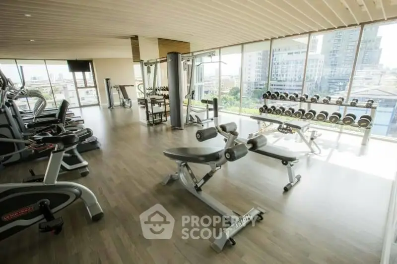 Spacious gym with modern equipment and city view in luxury apartment building.
