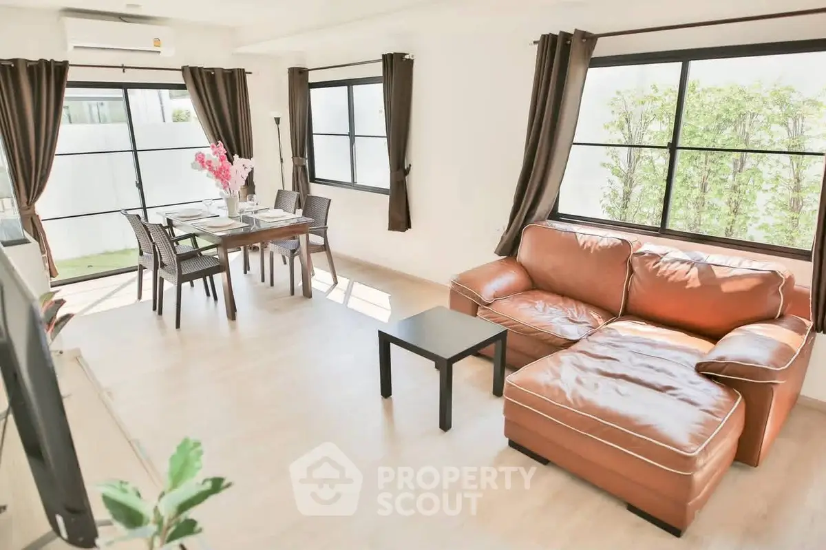 Spacious living room with leather sofa and dining area, large windows, and natural light.