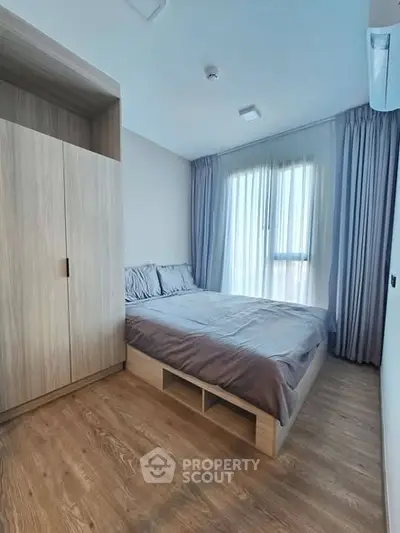 Modern bedroom with wooden flooring and large window for natural light.