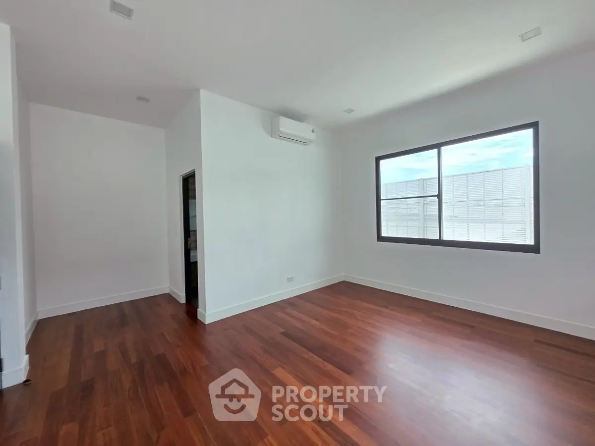 Spacious empty room with wooden floors and large window, ideal for customization.