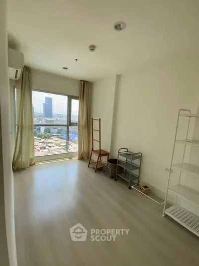 Bright room with large window offering city view, minimal furnishings, and light wood flooring.