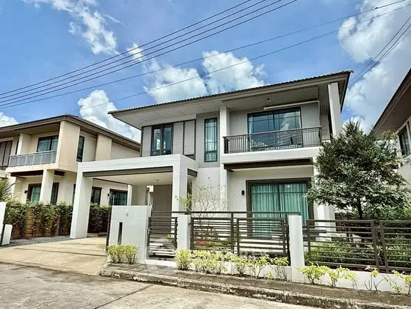 Modern two-story house with balcony and gated entrance under a clear blue sky.