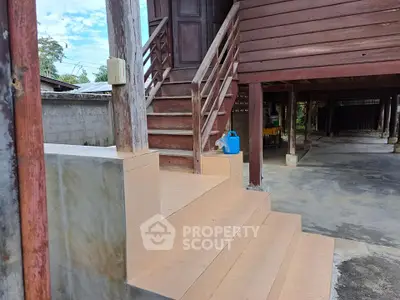 Traditional wooden house with elevated entrance and tiled steps, showcasing rustic charm and outdoor space.