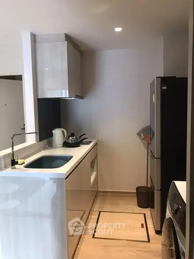 Compact modern kitchen with sleek white countertops, ample cabinetry, and full-sized black refrigerator, perfect for urban living.