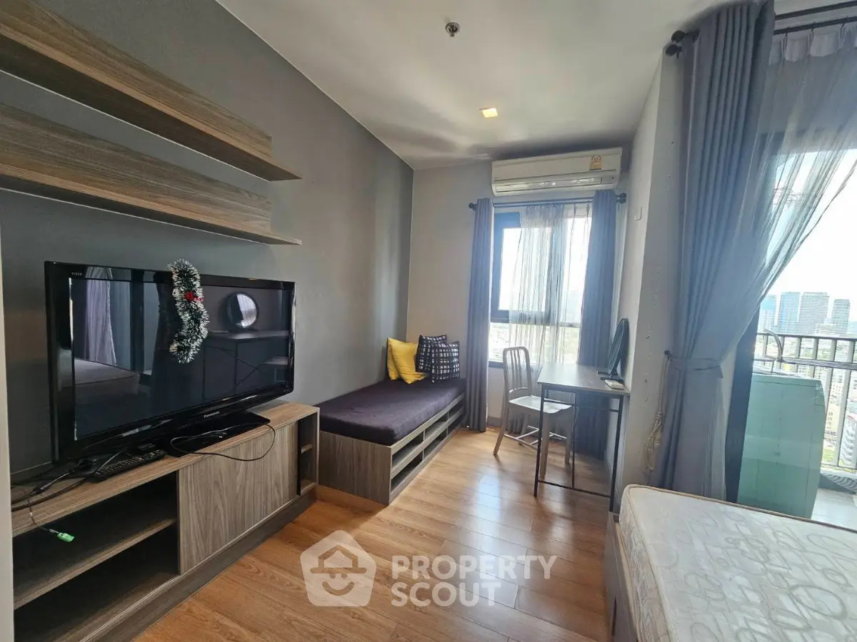 Modern living room with TV, cozy seating, and city view from balcony in stylish apartment.