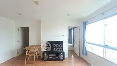 Bright living room with wooden flooring and large window, featuring a TV and dining area.