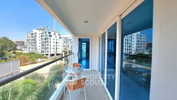 Spacious balcony with modern glass railing and outdoor seating, offering a stunning view of contemporary buildings.