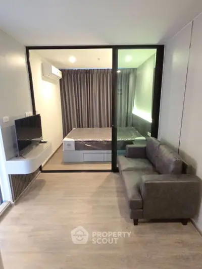 Modern studio apartment with glass partition, cozy sofa, and sleek TV setup.