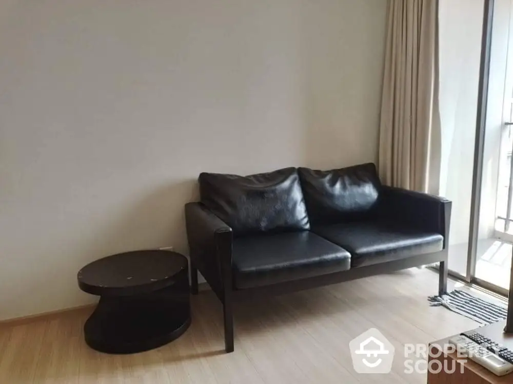 Modern living room with sleek black sofa and round side table near balcony.