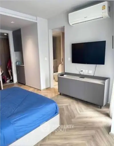 Modern bedroom with blue bedding, wall-mounted TV, and air conditioning unit.
