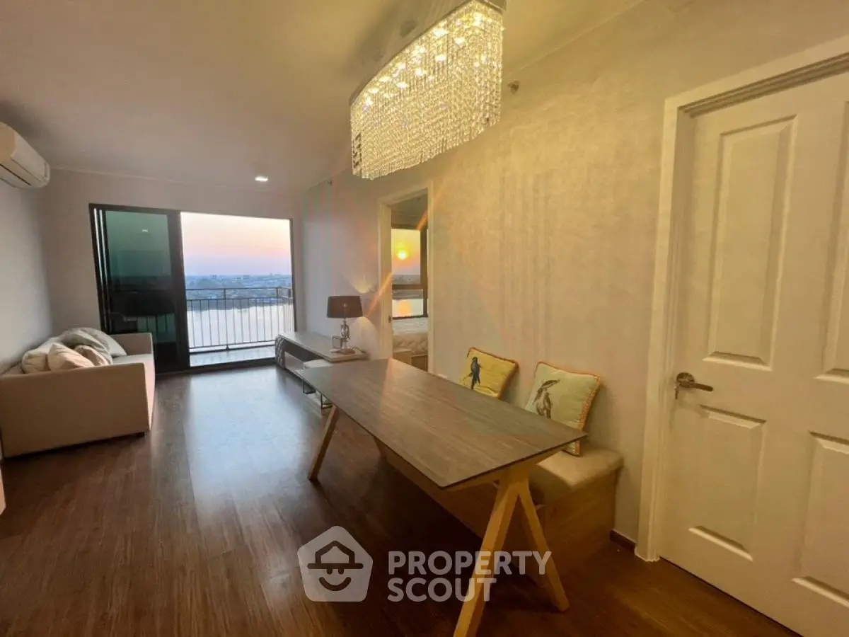 Modern living room with elegant chandelier and sunset view from balcony.