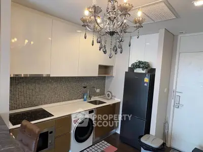 Modern kitchen with chandelier, washing machine, and sleek appliances in stylish apartment.