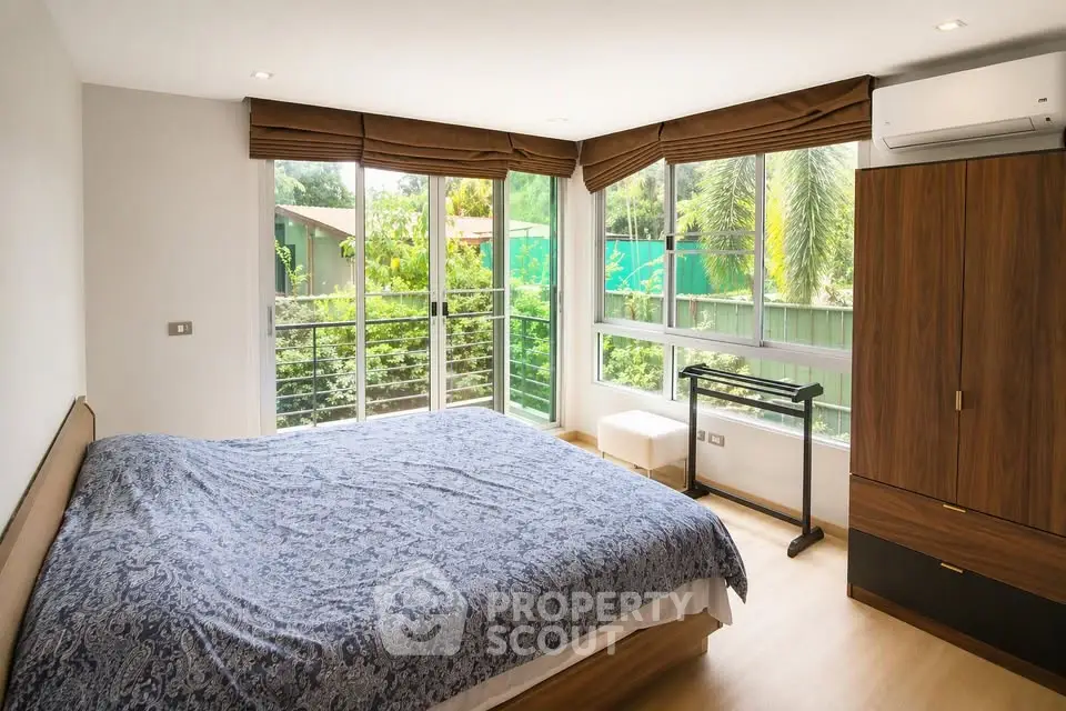Spacious bedroom with large windows and garden view, featuring modern furniture and air conditioning.