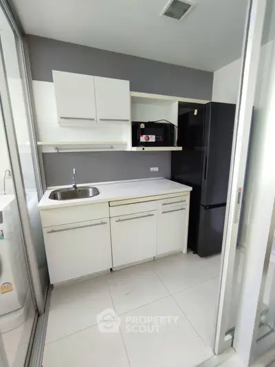 Modern compact kitchen with sleek white cabinets and stainless steel sink, ideal for urban living.