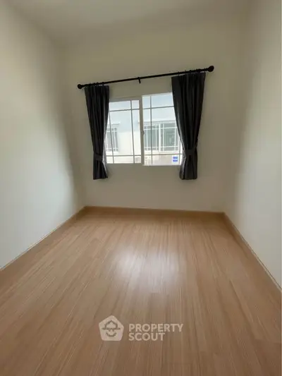Spacious empty room with wooden flooring and large window, perfect for customization.