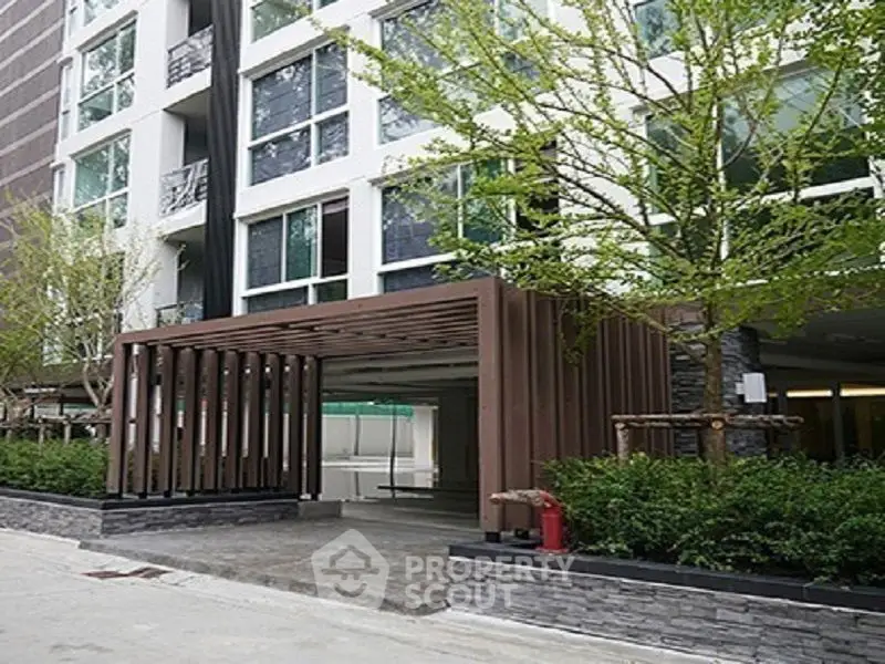 Modern apartment building entrance with sleek design and lush greenery.