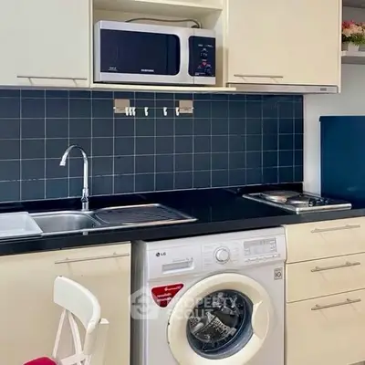 Modern kitchen with washing machine and microwave, sleek black countertops.