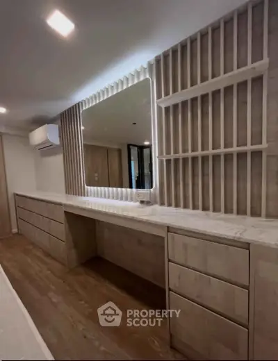 Modern bedroom with built-in wooden dresser and illuminated mirror