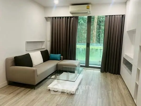 Modern living room with sleek sofa and glass coffee table, featuring floor-to-ceiling windows and lush garden view.