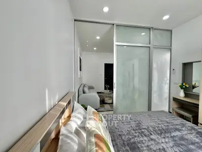 Modern bedroom with sliding glass doors and cozy living area, featuring stylish decor and ample natural light.