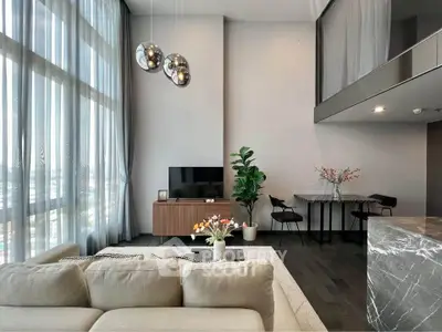 Modern living room with high ceilings, elegant decor, and large windows offering abundant natural light.
