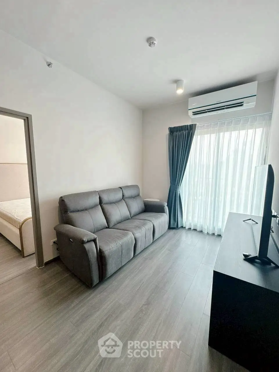 Modern living room with sleek gray sofa, air conditioning, and natural light from large window.