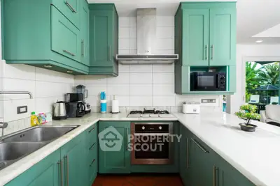 Modern kitchen with green cabinets, gas stove, and stainless steel appliances in a bright, airy space.