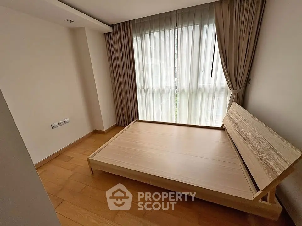 Spacious bedroom with wooden flooring and large window for natural light.