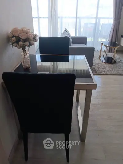 Modern living room with glass dining table and cozy seating area, featuring elegant decor and natural light.