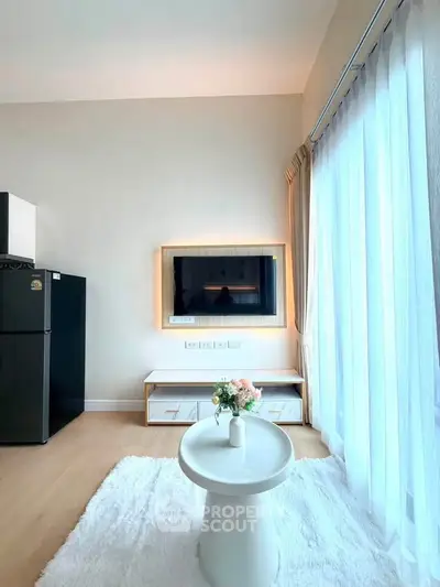 Bright living room with modern decor, featuring a large window, stylish furniture, and a sleek black refrigerator.