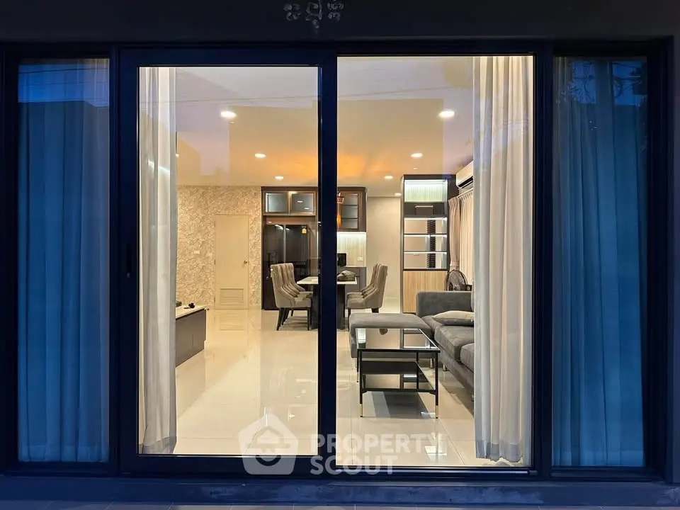 Luxurious modern living room with elegant decor and ambient lighting viewed through glass doors.